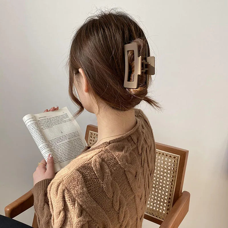 Woman with brown floral geometric hair claw clip, reading a book while seated in a cozy sweater.