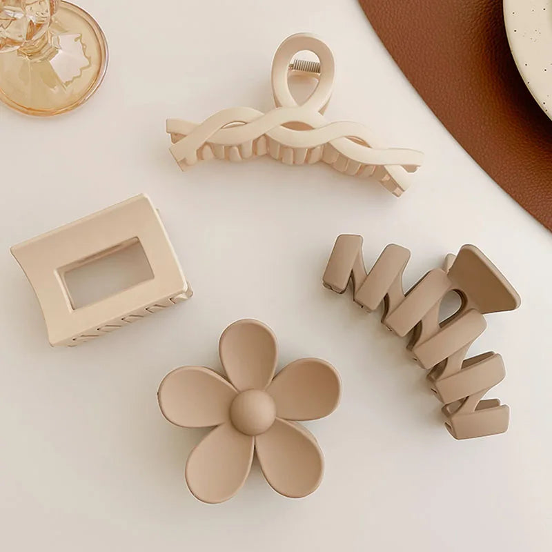 Collection of four stylish beige hair claws in various designs, including a flower and geometric shapes, on a light surface.