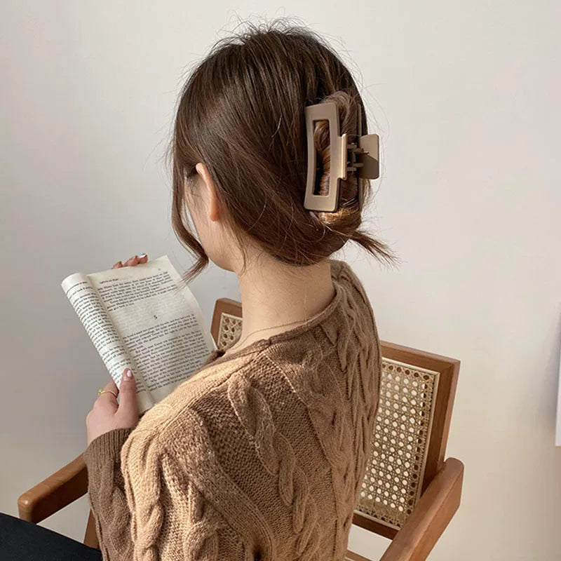 Woman with brown geometric floral hair claw reading a book, showcasing elegant hairstyle in neutral tones.